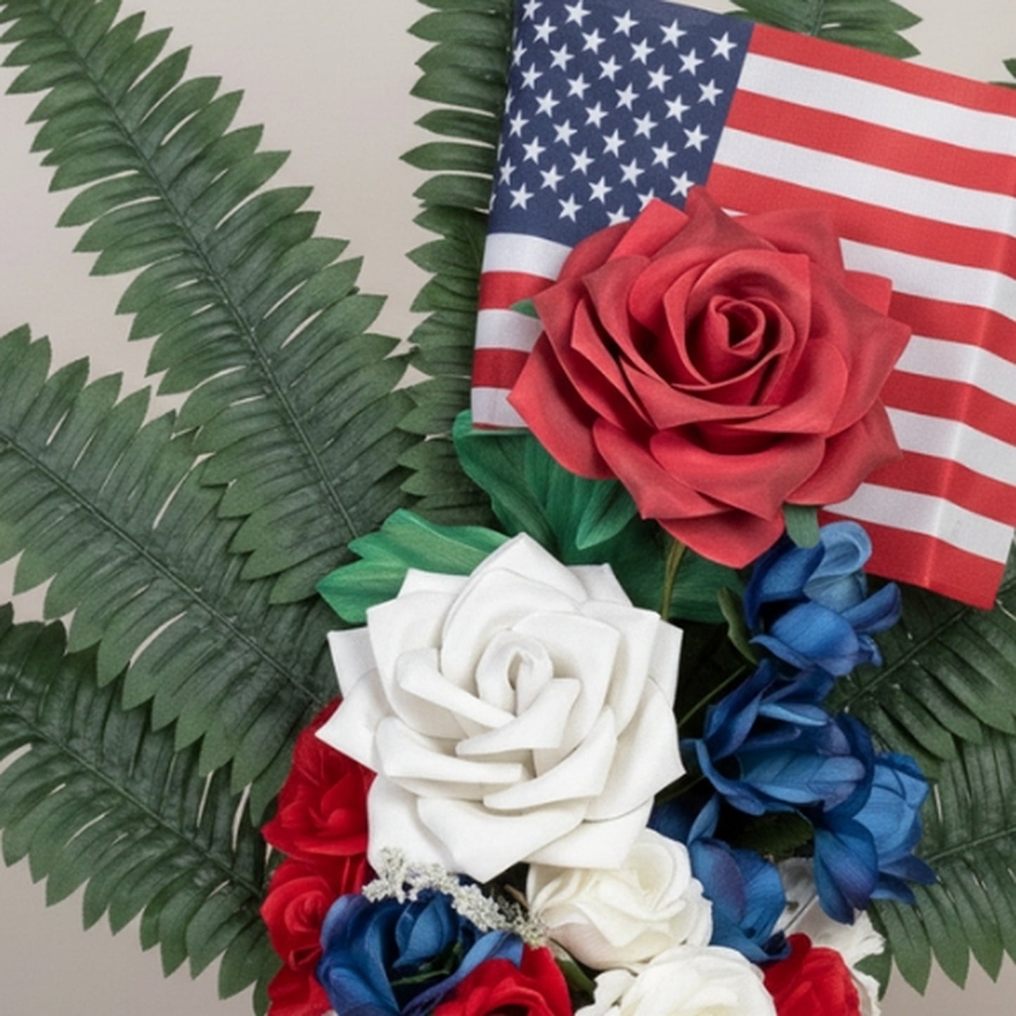 Detailed close-up of patriotic artificial rose bouquet showcasing large red and white foam roses with royal blue accent flowers, American flag, dark green fern fronds, and baby's breath filler - high-quality memorial flower arrangement for patriotic occasions

Keywords: patriotic roses close-up, artificial flower detail, memorial bouquet, red white blue flowers, American flag arrangement, foam roses