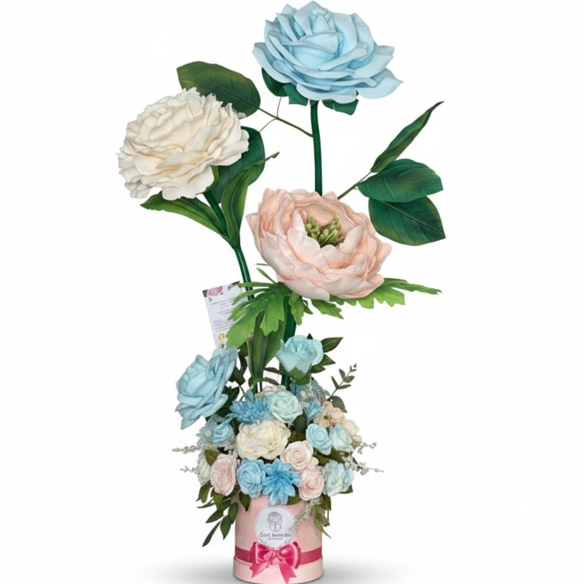 Professional studio photograph of an elegant tall floral arrangement in a light pink cylindrical hatbox with dark pink satin ribbon bow and white circular logo. Three giant oversized flowers rise on long green stems: a large light blue rose at the top, a creamy off-white peony to the left, and a soft peachy-pink peony with green center to the right. The base contains a lush bouquet of smaller pastel blue, pale pink, and cream flowers including roses, carnations, and chrysanthemums with green foliage. Pure w