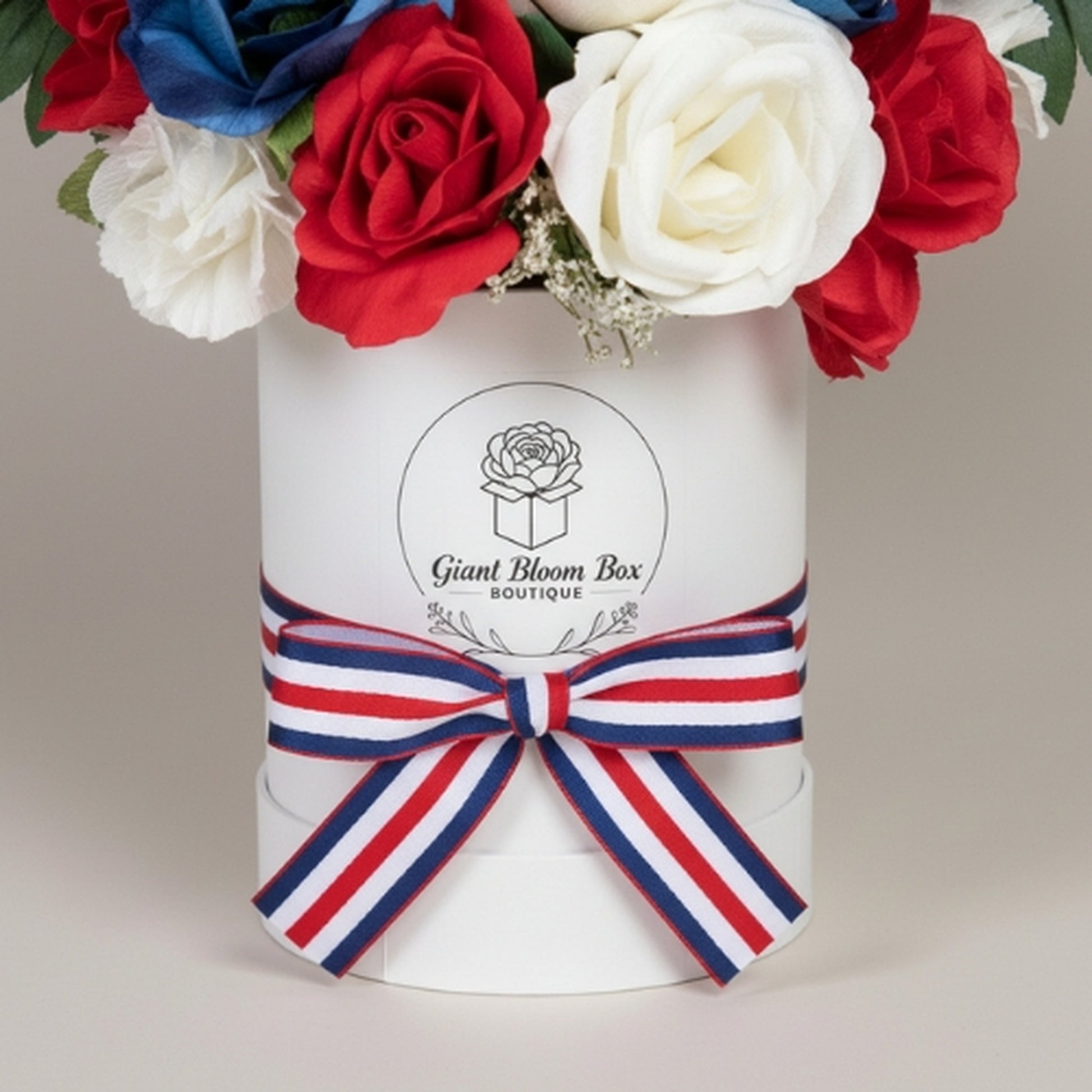 Premium patriotic floral arrangement in white cylindrical Giant Bloom Box boutique container featuring dense dome of red, white, and royal blue artificial roses with baby's breath, branded logo, and striped grosgrain ribbon bow - luxury gift for Memorial Day, Veterans Day, or Independence Day

Keywords: Giant Bloom Box, luxury patriotic flowers, bloom box arrangement, branded flower gift, premium artificial roses, patriotic gift box